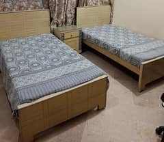 Two beds with mattresses and a side table