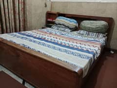 wooden double bed with mattress and side table.