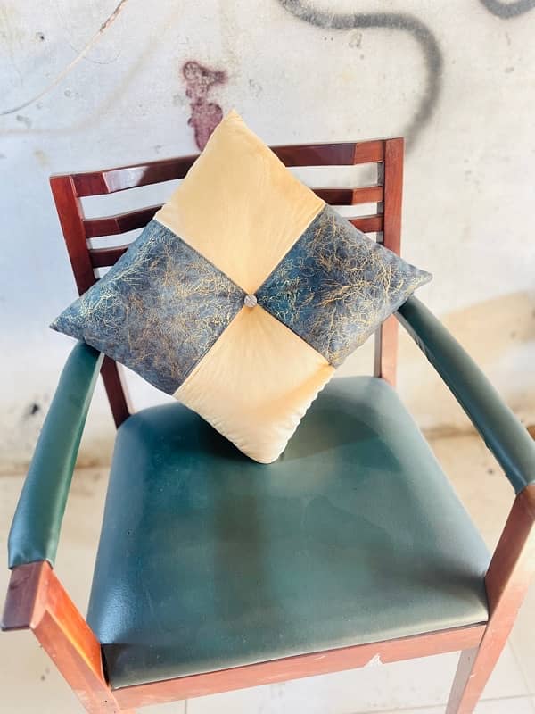 A beige and cream-green square cushion rests on a chair. 0