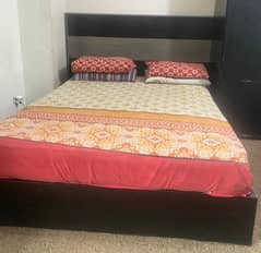 Queen sized bed with one side table wooden cupboard and dressing table