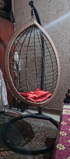 hanging swing chair with two red cushions and a iron stand