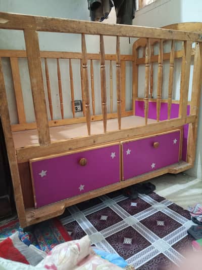 Wooden baby cot with pinkish purple cabinet below