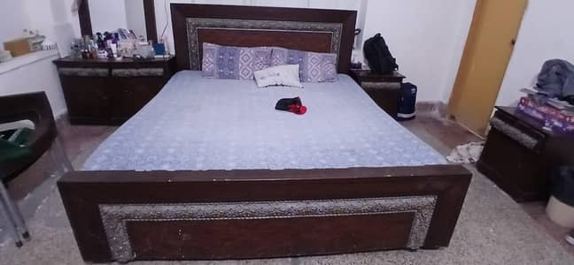 wooden bed with mattress, side table and dressing table
