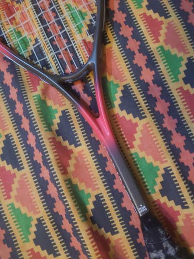 This is a black and red graphite squash racquet with a long grip.