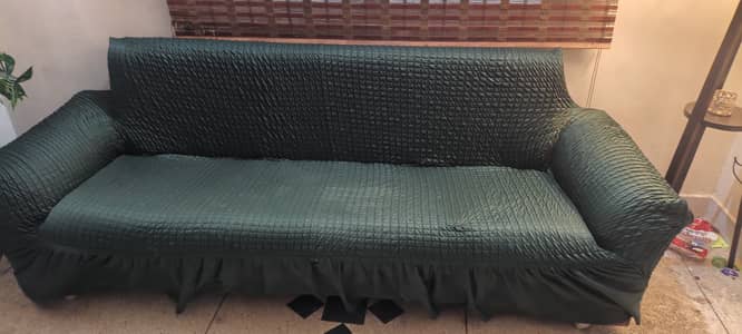 A sofa cum bed with a green cover and storage space underneath th